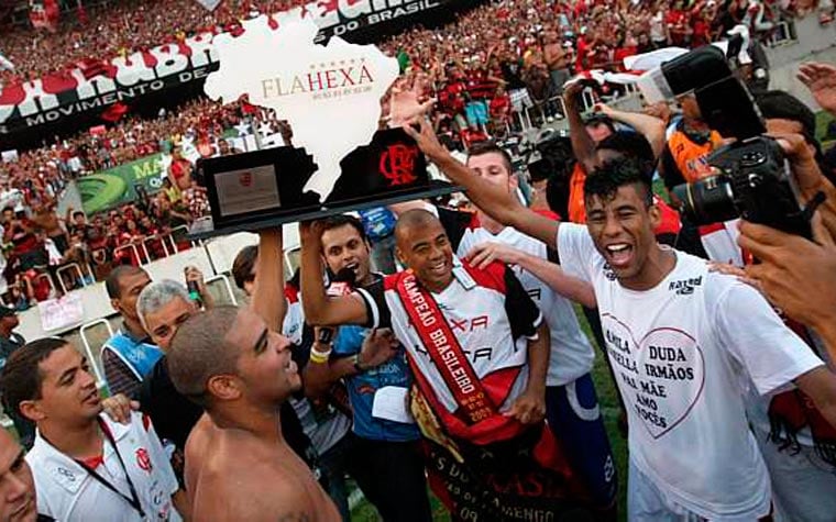 Fotografia real de Adriano Imperador, Dejan Petkovic, Ronaldo Angelim, Bruno, Léo Moura, Juan e Andrade celebrando o Hexacampeonato Brasileiro em 6 de dezembro de 2009 no Maracanã. Na aba '📰 Recorte de Jornal', confira a capa real digitalizada do Diário Lance! de 7 de dezembro de 2009. (Fonte Oficial: Diário Lance! & Acervo O Globo (Fotos e Capas Originais de 2009) · Agência Lancepress! & Acervo O Globo)