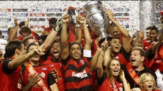 Fotografia real do elenco rubro-negro erguendo o troféu de Campeão Carioca Invicto de 2011 após superar o Vasco na decisão da Taça Rio (Foto: Gilvan de Souza / Lancepress!). Com Ronaldinho Gaúcho marcando de falta na final da Taça Guanabara e dando show no clássico épico de 5 a 4 sobre o Santos na Vila Belmiro, 2011 ficou na memória. (Fonte Oficial: Diário Lance! / Agência Lancepress! · Gilvan de Souza / Agência Lancepress!)