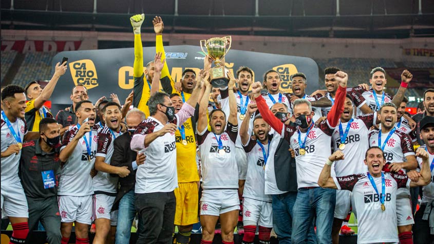 Fotografia real do elenco rubro-negro erguendo a taça do 37º Campeonato Carioca (6º Tricampeonato Estadual da história do clube: 2019-2020-2021) após vencer o Fluminense por 3 a 1 na final no Maracanã, com dois gols de Gabigol e um de João Gomes (Foto: Alexandre Vidal / Acervo Lance!). Em abril, o time já havia batido o Palmeiras nos pênaltis pela Supercopa do Brasil. (Fonte Oficial: Diário Lance! & Acervo O Globo · Alexandre Vidal / CRF & Armando Paiva (Lancepress!))
